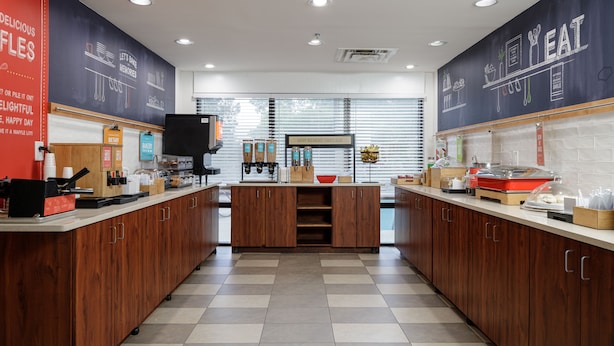 A modern kitchen with wooden cabinets, a central island, and a chalkboard wall with food-related drawings. - Hampton Inn Bellevue / Nashville-I-40 West (Nashville)
