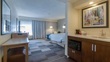 Habitación de hotel con cama, escritorio, baño con lavamanos y una gran fotografía enmarcada de un paisaje urbano en la pared.