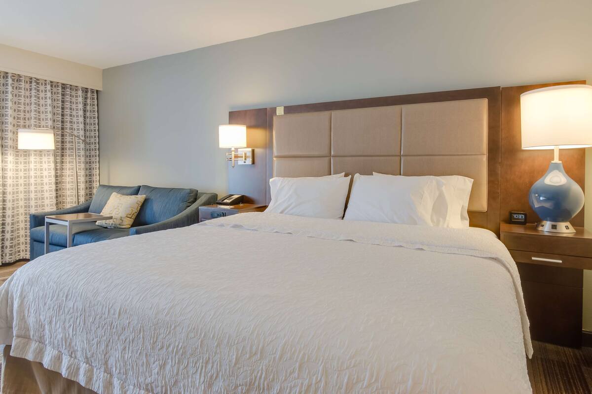 Habitación de hotel con una cama grande, un sofá, un escritorio con lámpara y una mesita de noche con teléfono.