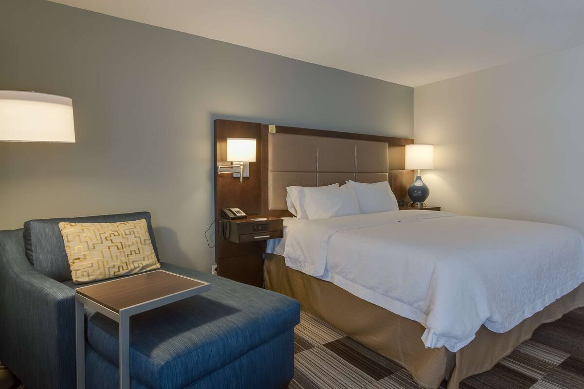 Una habitación de hotel con cama, una silla, una mesita de noche y una lámpara.