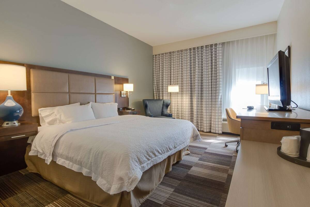 Una habitación de hotel con una cama grande, un escritorio con una computadora, una silla y un televisor.