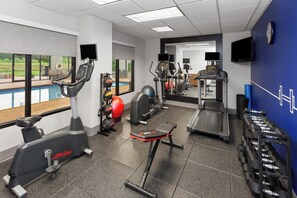 A gym with cardio equipment, weights, and a pool view.