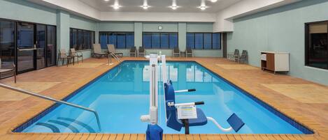 An indoor swimming pool with a lifeguard chair, a pool ladder, and a safety sign.