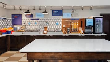Uma área de café da manhã moderna com ilha central, balcão de café e diversos dispensadores de alimentos e bebidas.