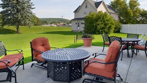 Une terrasse avec une table ronde et des chaises, un pot de fleurs et une maison en arrière-plan.