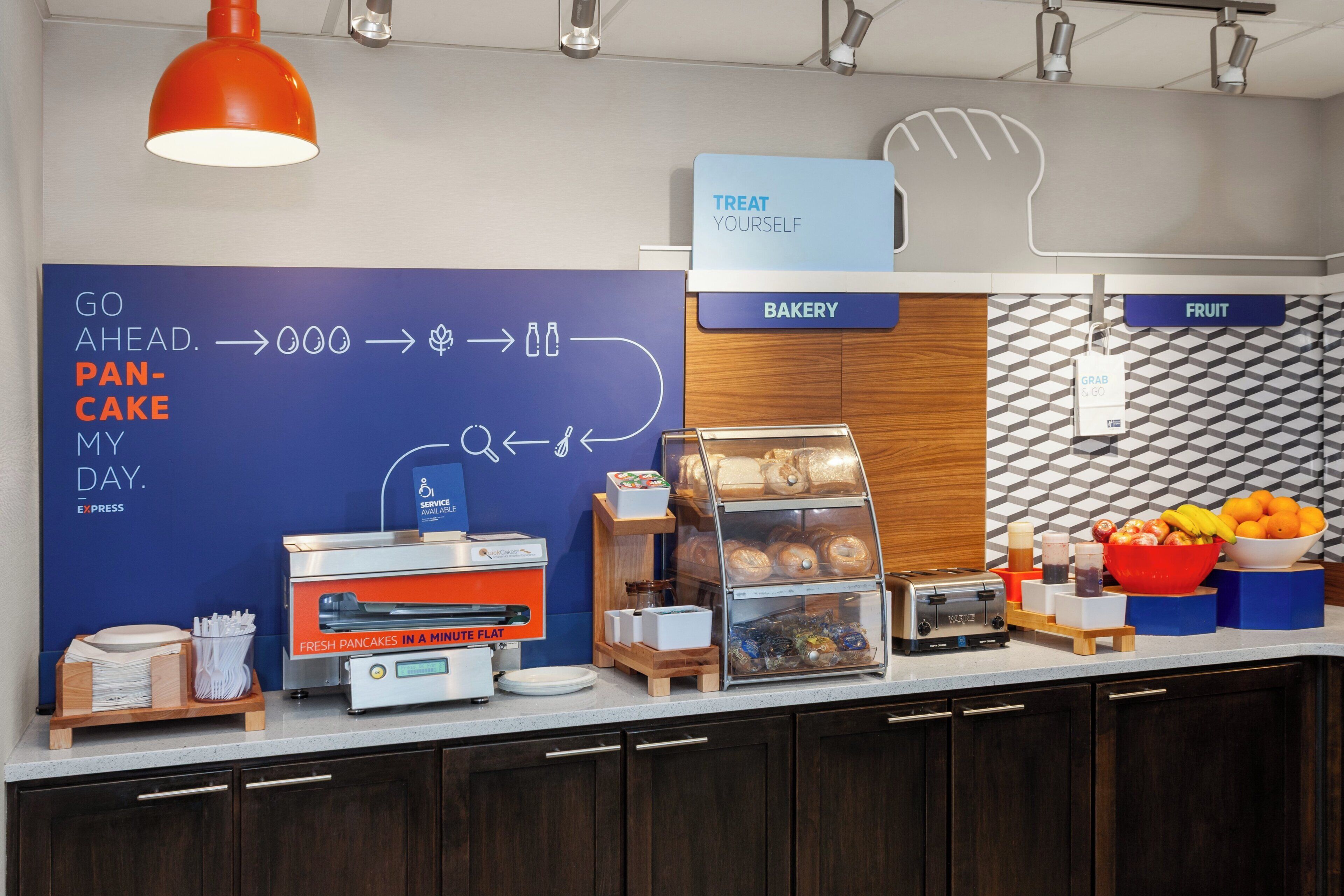 A breakfast area with a sign indicating a self-serve option, a display of fresh pastries, and a toaster.