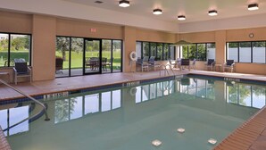 Une piscine intérieure avec des parois en verre transparent, une terrasse carrelée et quelques chaises longues.