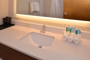 A hotel bathroom with a white sink, a mirror, and a towel rack with towels.