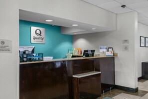 A hotel reception area with a teal-colored wall, a sign indicating 'Quality by Choice Hotels,' a non-smoking sign, and a check-in/out sign. - Quality Inn Cleveland, MS (Cleveland)