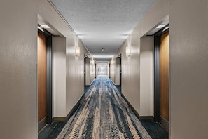 A hotel hallway with carpeted floors, doors on both sides, and wall-mounted lighting. - Quality Inn Cleveland, MS (Cleveland)
