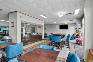 Un comedor de hotel con mesas y sillas, una zona de cocina y un televisor en la pared.