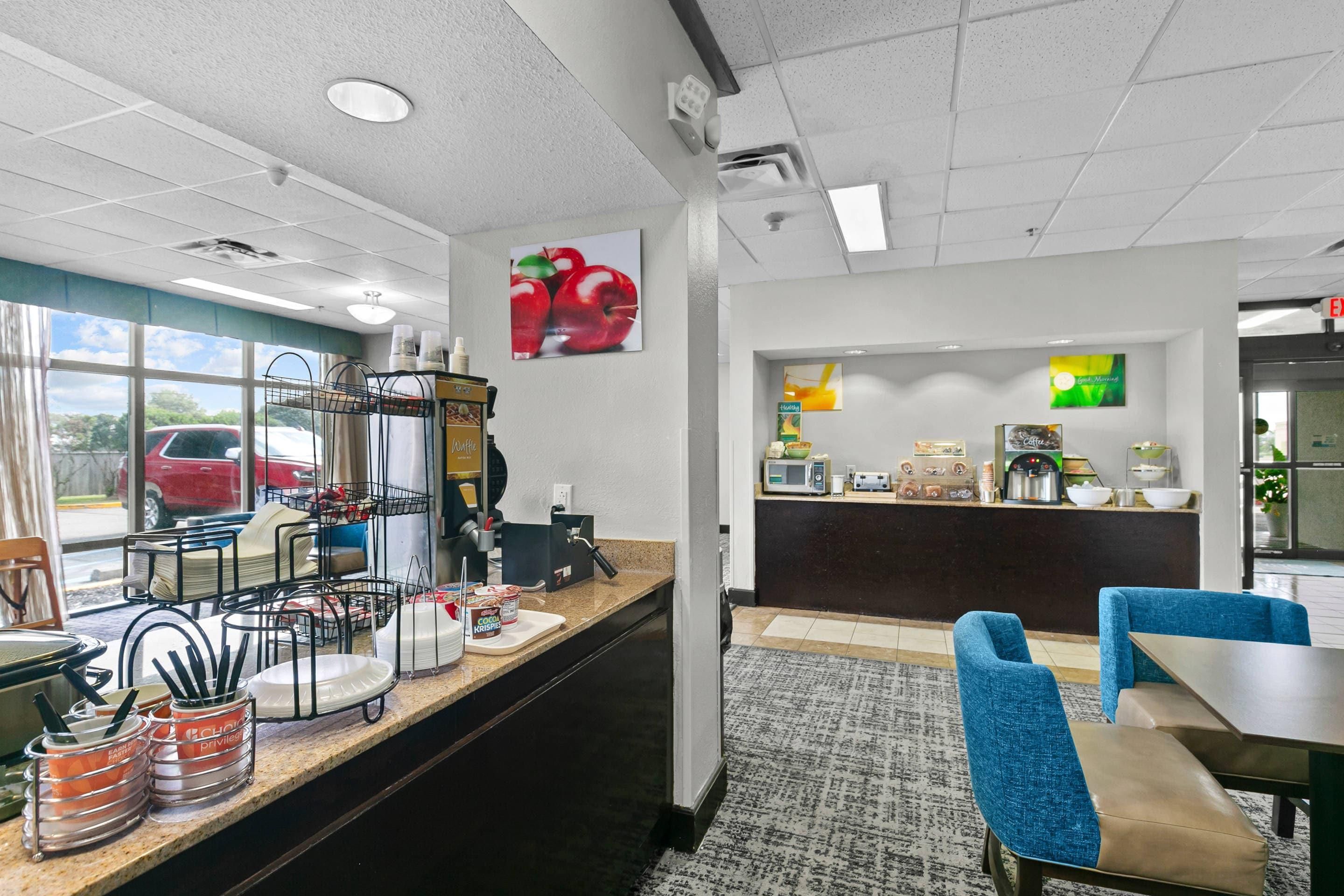A hotel breakfast area with a counter, seating, and a view of the parking lot.