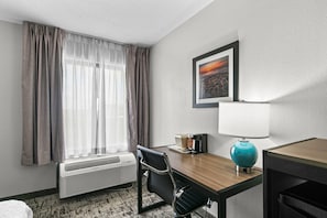 A hotel room with a desk, chair, air conditioning unit, a coffee maker, a framed picture on the wall, and a window with curtains. - Quality Inn Cleveland, MS (Cleveland)