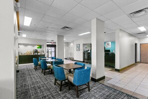 Un comedor de hotel con mesas y sillas, un mostrador de recepción y una zona de cocina.