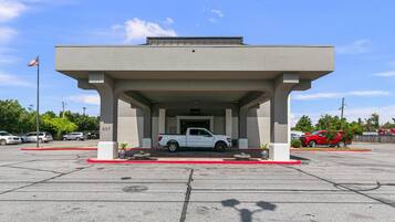 A building with a covered parking area, a white pickup truck parked inside, and a red car parked outside.