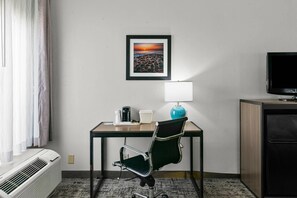 Habitación de hotel con escritorio, silla, televisor y un cuadro en la pared.