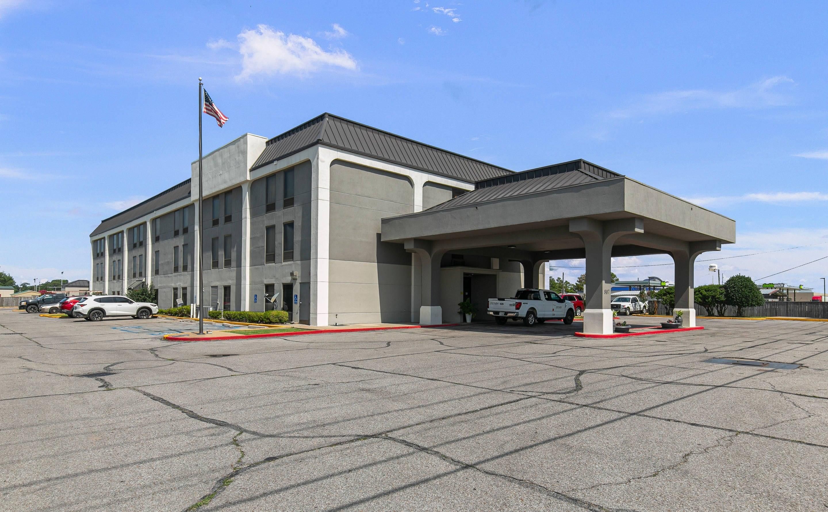 A building with a covered parking area, a flag, and a truck.