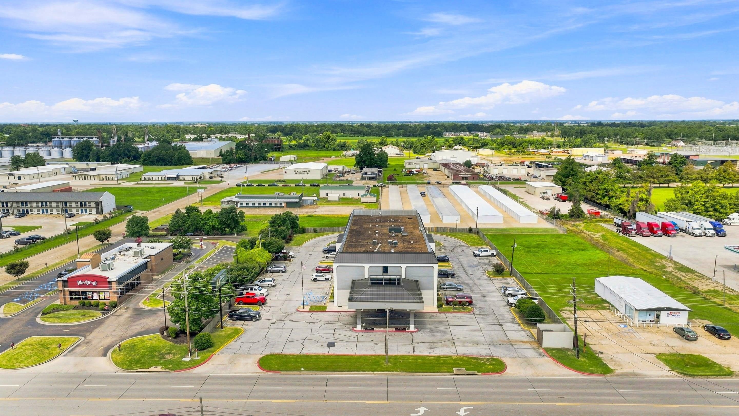 A commercial area with a large parking lot, a building with a flat roof, and several industrial structures.