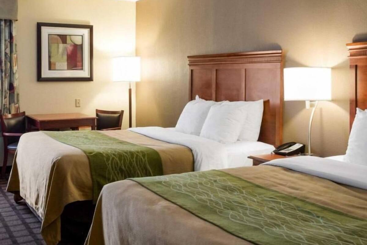A hotel room with two beds, a desk, a chair, a lamp, and a framed picture on the wall.