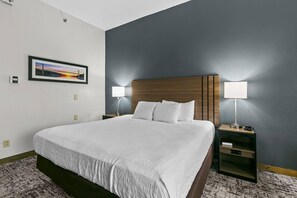 Una habitación de hotel con una cama grande, dos mesitas de noche con lámparas, un cuadro enmarcado en la pared y un termostato.