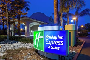 Señal de Holiday Inn Express & Suites, con una vista despejada de la entrada del hotel y palmeras al fondo.