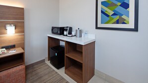 Une chambre d’hôtel équipée d’une kitchenette, d’un four à micro-ondes, d’une machine à café, d’un réfrigérateur, d’une petite table avec un téléphone et des documents, d’un tableau abstrait encadré et d’un banc en bois.
