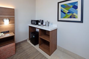 Une chambre d’hôtel équipée d’une kitchenette, d’un four à micro-ondes, d’une machine à café, d’un réfrigérateur, d’une petite table avec un téléphone et des documents, d’un tableau abstrait encadré et d’un banc en bois.