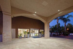 A hotel entrance with a covered patio, large windows, and potted plants.