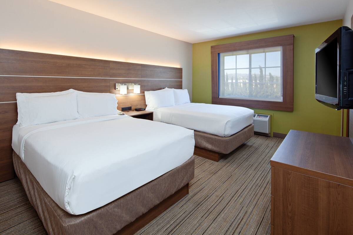 Habitación de hotel con dos camas, televisión, ventana y cabecero de madera.