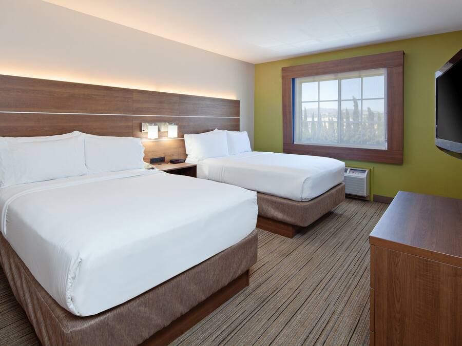 Habitación de hotel con dos camas, televisión, ventana y cabecero de madera.