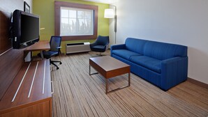 Une chambre d’hôtel avec une télévision, un canapé bleu, un bureau en bois, une chaise et une lampe.