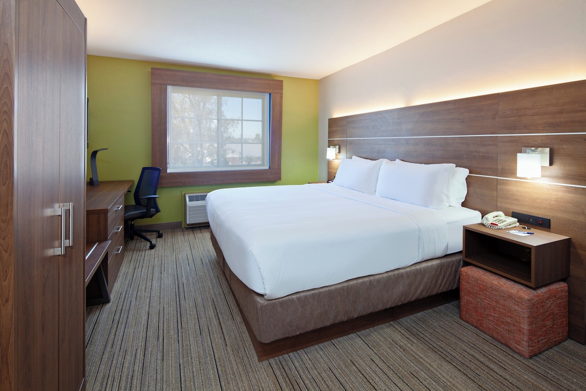 Une chambre d’hôtel avec un grand lit, un bureau, une chaise de bureau, une fenêtre, une table de chevet et un téléphone.