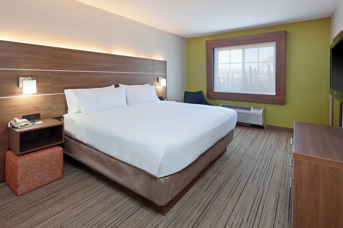 Une chambre d’hôtel avec un grand lit, des lampes de chevet, une petite table avec un téléphone, une fenêtre et un téléviseur.