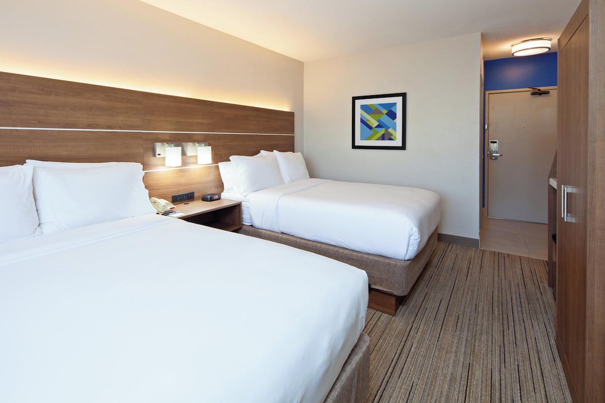 Une chambre d’hôtel avec deux lits, une table de chevet avec une lampe, un tableau encadré au mur et une porte donnant sur une salle de bain.