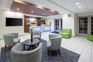 A lobby with a reception desk, seating area with chairs, a flat-screen TV, and a green sofa.