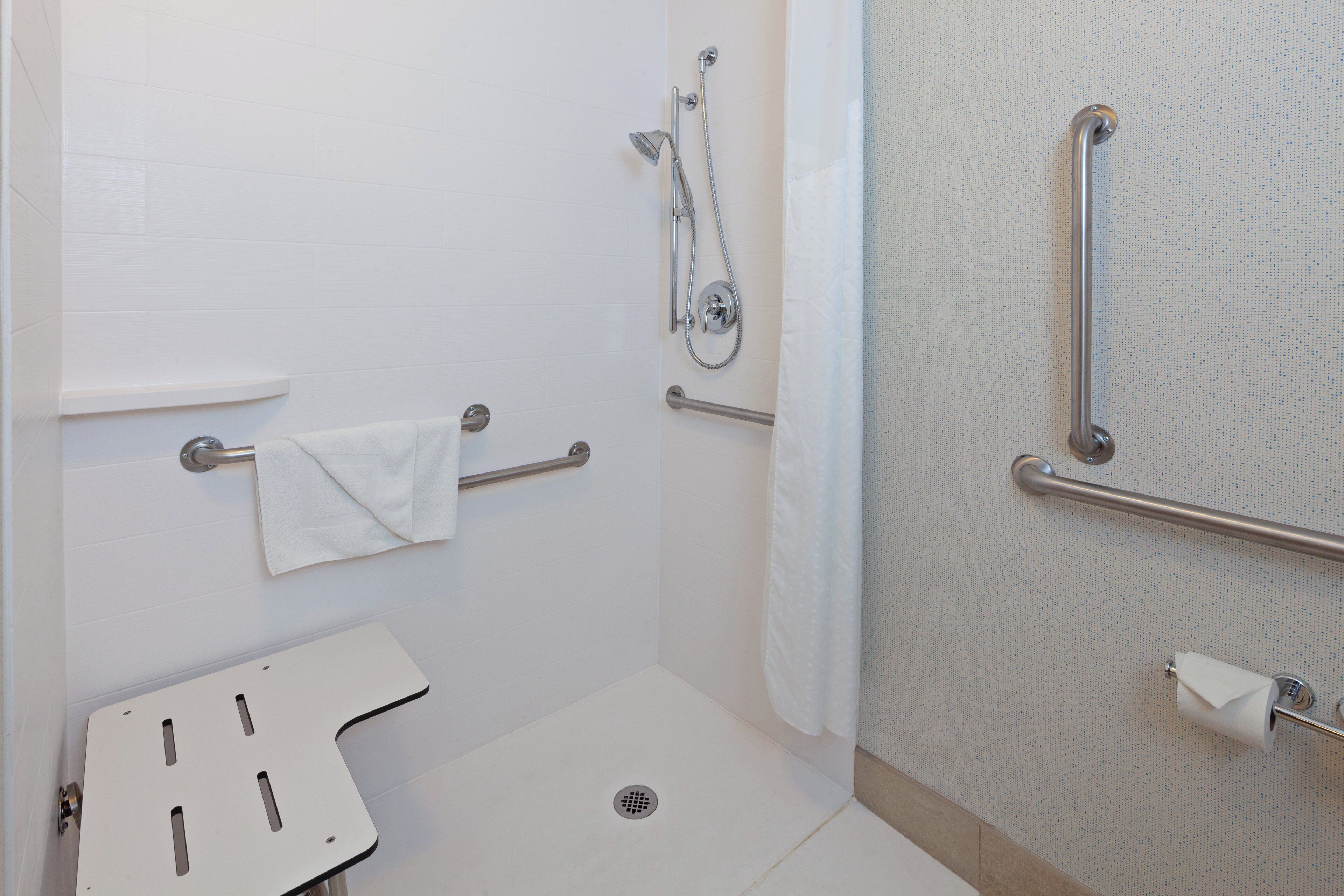 A shower area with a grab bar, a towel rack, and a white sink.