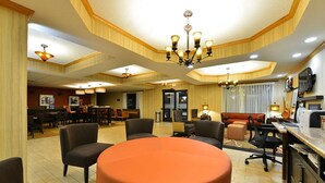 A hotel lobby with a round orange table, multiple seating areas, a dining section, and a television mounted on the wall. - Hampton Inn Sturgis-Lagrange Area (Sturgis)