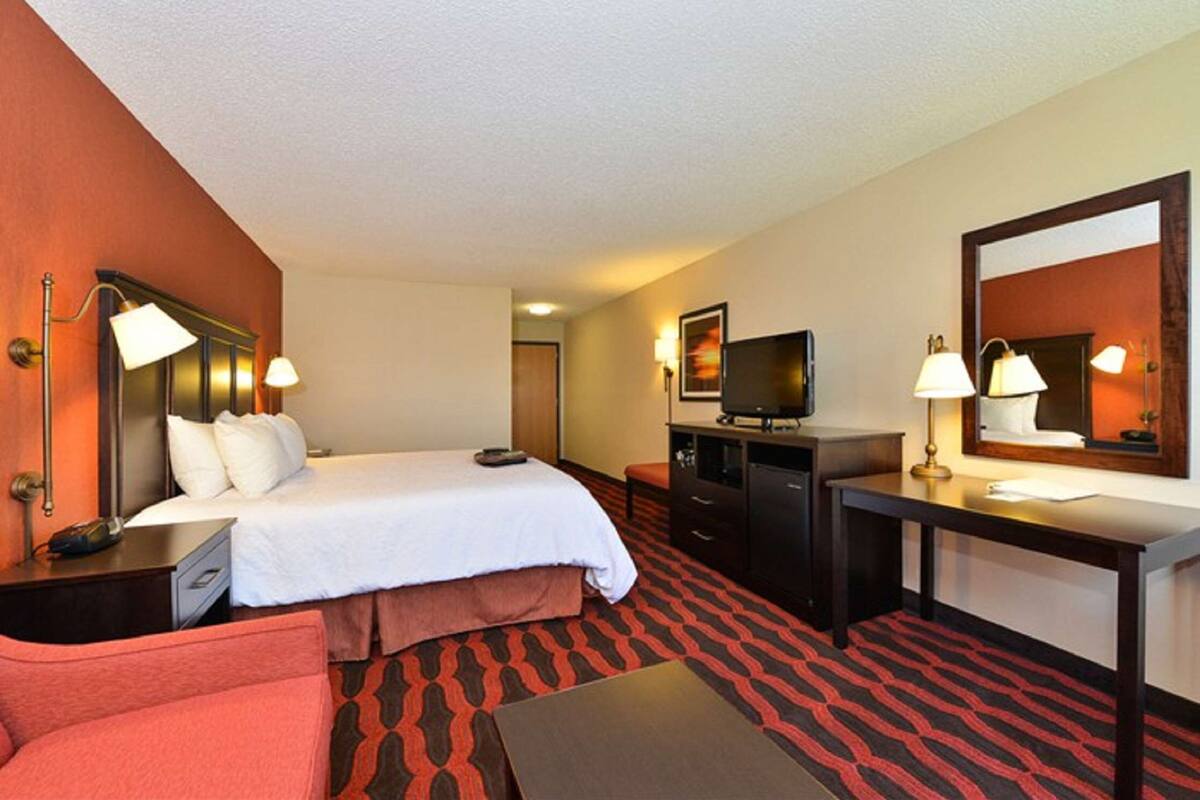 A hotel room with a bed, a desk, a television, and a mirror.