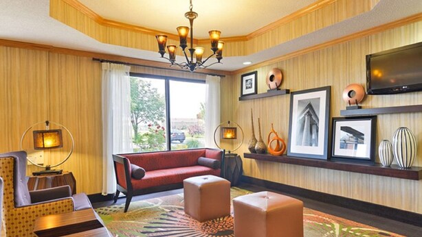 A hotel room with a red sofa, ottomans, a chandelier, a flat-screen TV, and framed pictures on the wall. - Hampton Inn Sturgis-Lagrange Area (Sturgis)