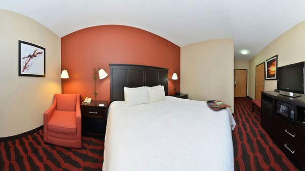 A hotel room with a large bed, a red armchair, a desk with a lamp, a television, and a framed picture on the wall. - Hampton Inn Sturgis-Lagrange Area (Sturgis)