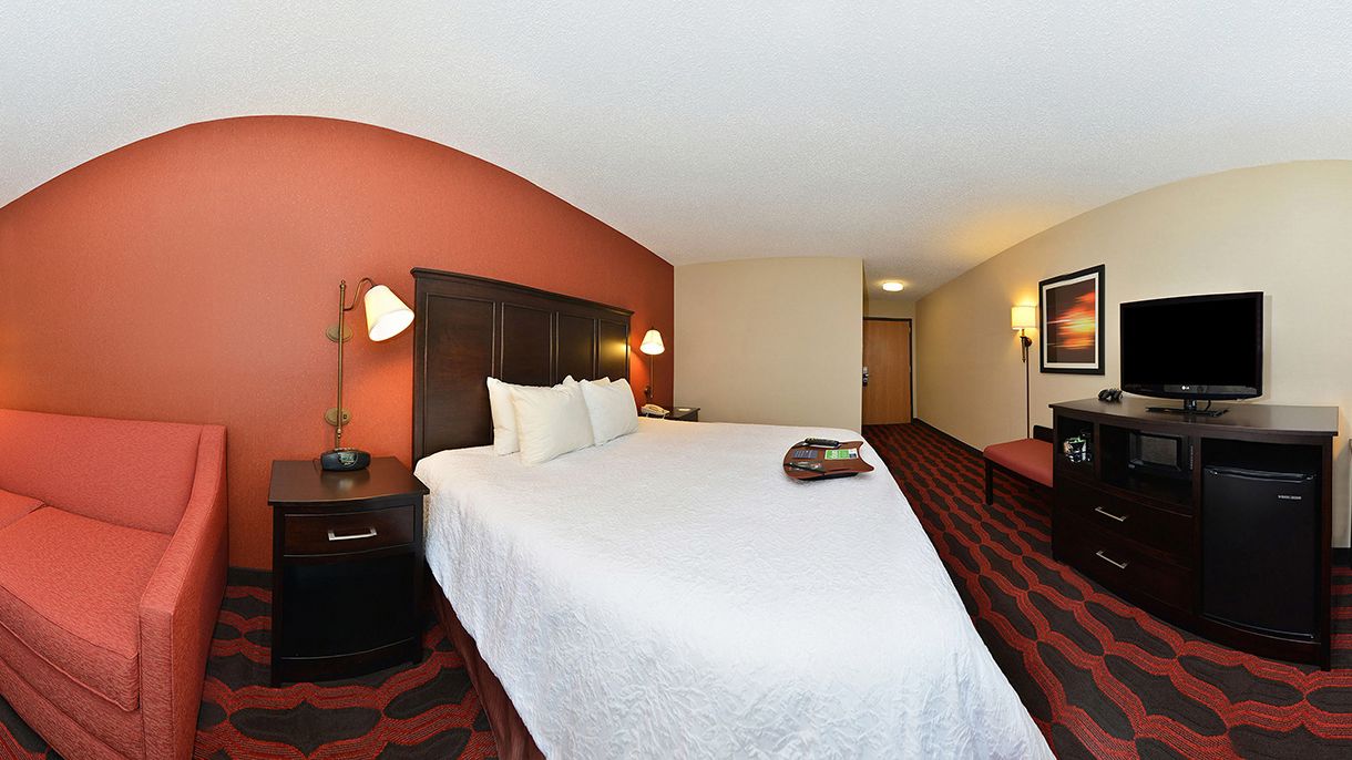 Een hotelkamer met een groot bed, een bureau, een stoel, een televisie en een dressoir.