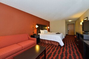 A hotel room with a bed, a red sofa, a desk, and a television.