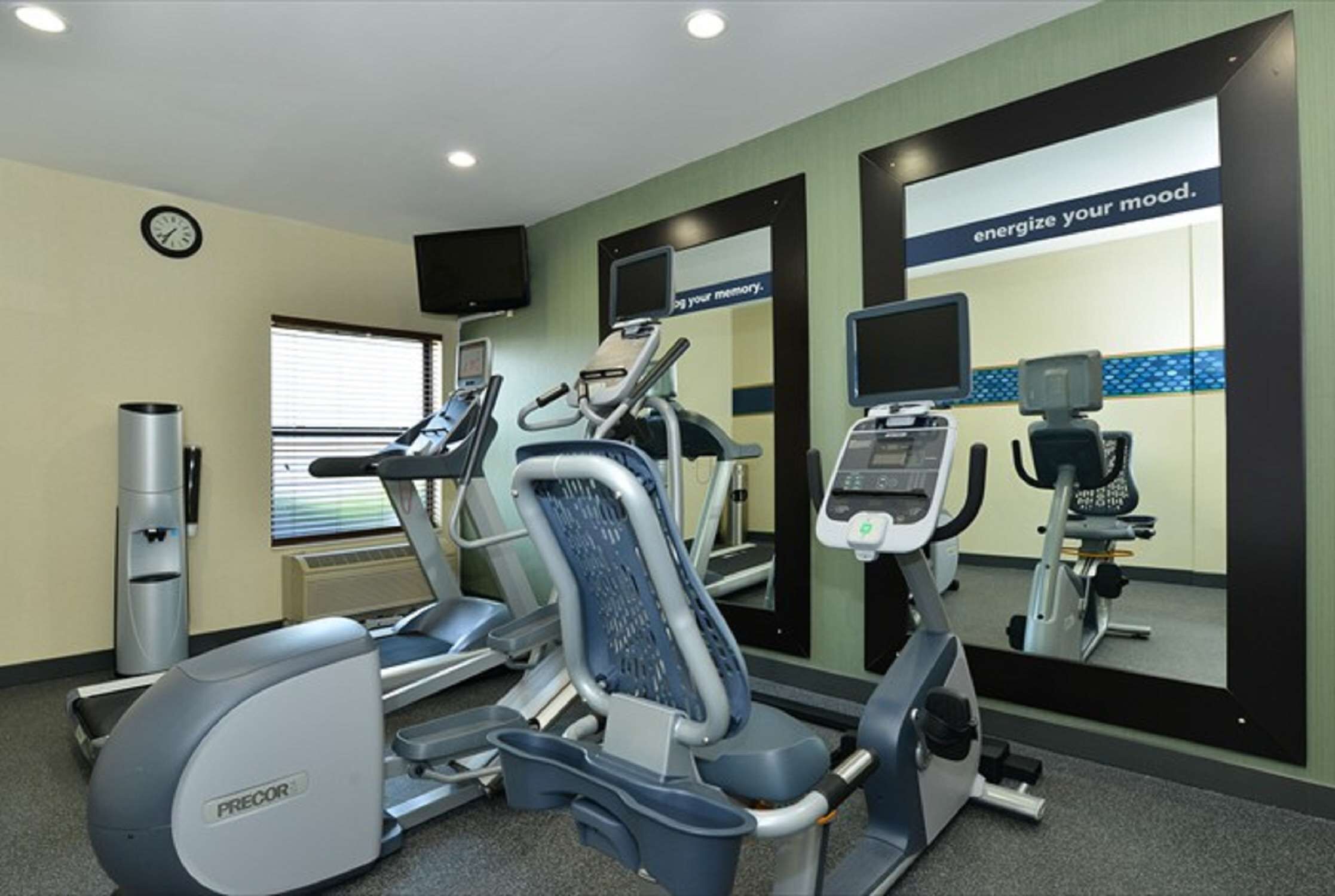A gym with treadmills, elliptical machines, and a mirrored wall with motivational text.