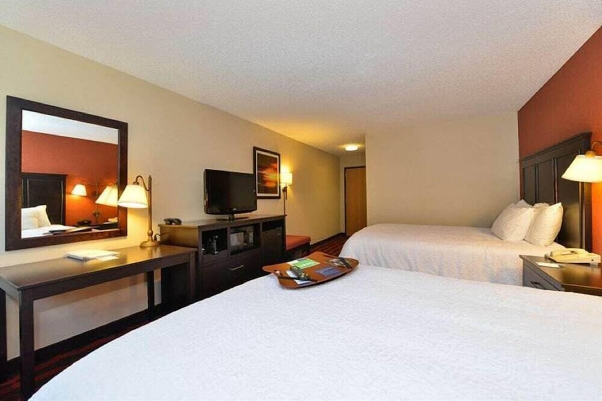 A hotel room with two beds, a desk, a television, and a mirror.