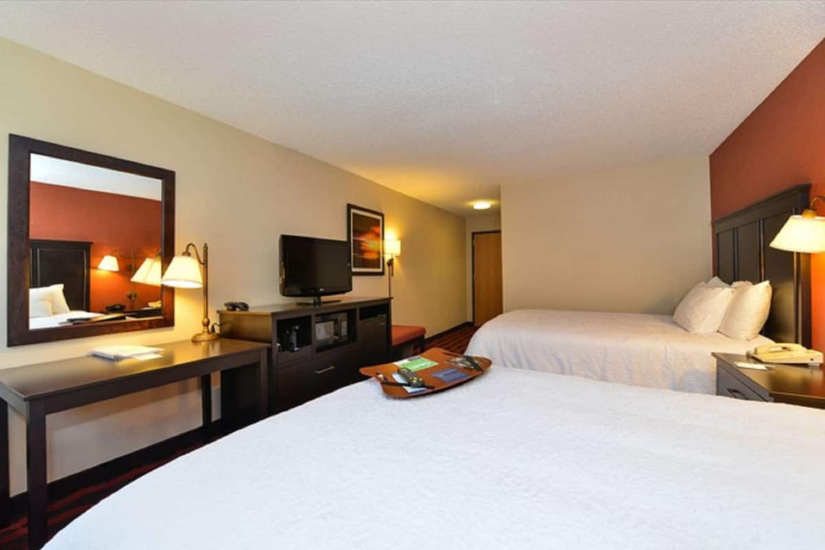 A hotel room with two beds, a desk with a flat-screen TV, a mirror, and bedside lamps.