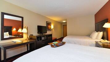 A hotel room with two beds, a desk with a flat-screen TV, a mirror, and bedside lamps.