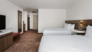 A hotel room with a bed, bedside table, lamp, and a television on a desk.