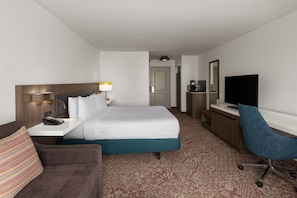 A hotel room with a bed, a desk, a TV, a chair, a lamp, and a small kitchenette. - Hilton Garden Inn Portland Airport (Portland)