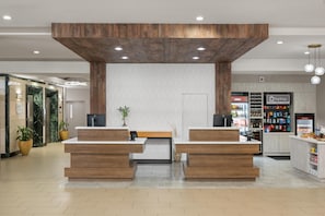 A reception area with a wooden reception desk, a potted plant, and a wall with a wavy pattern.