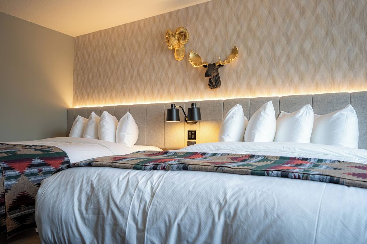 Une chambre d’hôtel avec deux lits, un mur décoré de motifs et des têtes d’animaux fixées au mur.